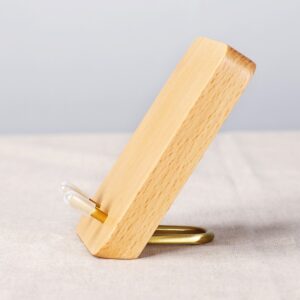 Side view of the pale beech wooden phone stand leaning on a brass loop foot, two pegs at the front
